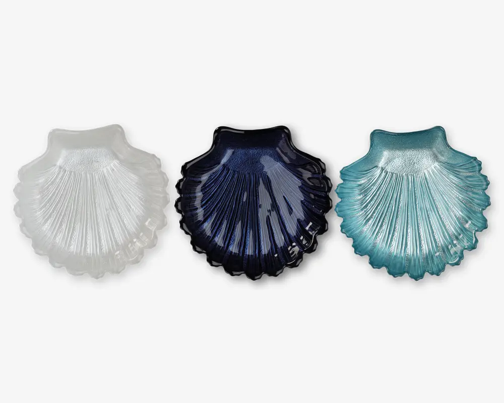 Sæt med tre skålformede fade i glas, hver med en rillet, tekstureret overflade, der efterligner en kammuslingskal. Sættet indeholder én skål i gennemsigtig hvid, én i mørkeblå og én i lyseblå/aquafarvet. Hver skål har en blank overflade og let hævede kanter, velegnet til servering af småting eller som dekorative elementer.