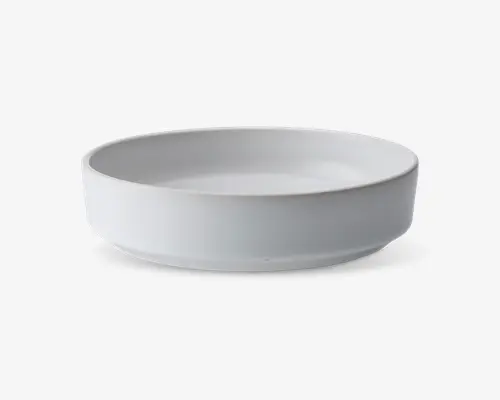 En rund, lav skål med en glat mat hvid overflade. Skålen har lige sider og en flad bund, hvilket giver et moderne og minimalistisk udtryk. Kanten er let afrundet for komfort og stil.