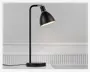 En moderne bordlampe med mat sort finish, rund fod, lige lodret stang og en vippet, kuppelformet skærm. Lampen har et minimalistisk design med synlig ledning og en metal-detalje ved samlingen mellem skærm og stang. Skærmen kan justeres, så lysets retning kan ændres.