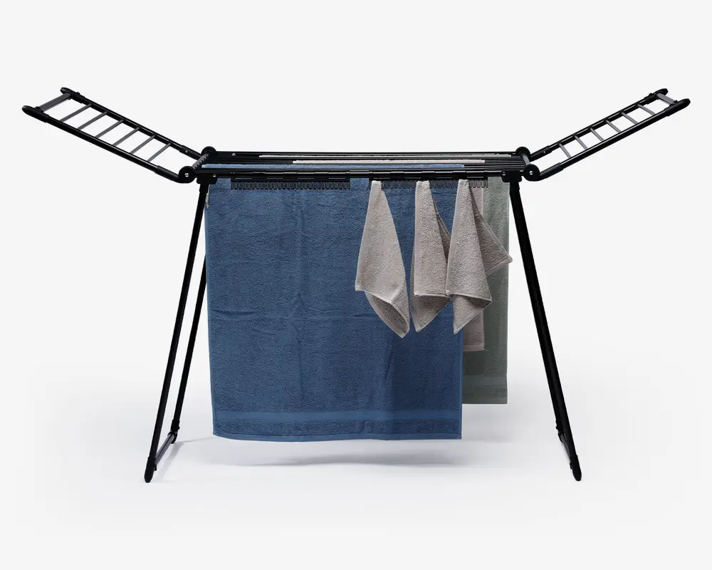 Et sammenklappeligt tørrestativ med en robust metalramme, der har to udtræksarme med flere stænger til ophængning af tøj. Stativet viser flere håndklæder i forskellige størrelser og farver, hvilket demonstrerer kapaciteten til både store og små genstande. Benene er vinklet for stabilitet, og designet sikrer effektiv luftcirkulation omkring det hængende vasketøj.
