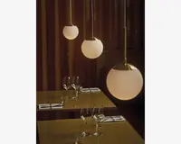 Tre kugleformede pendellamper med matteret glas og messingbeslag hænger i forskellige højder og udsender et varmt, blødt lys. Lamperne har et moderne, minimalistisk design med glatte overflader og rene linjer, velegnet til nutidige indretninger.