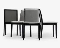 Sæt med fire moderne stole med lige ryg og firkantede sæder. Stolene har en slank sort træramme og er polstret med lysegråt stof på både sæde og ryglæn. Designet er minimalistisk og stolene kan stables, hvilket gør dem velegnede til spise- eller konferencelokaler.