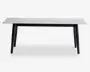 Rektangulært bord med en glat, hvid bordplade, der har et diskret marmorlignende mønster. Bordet har fire let skråtstillede, solide sorte ben, hvilket giver det et moderne og minimalistisk udtryk. Bordpladens kanter er lige og rene, og det samlede design er slankt og nutidigt.