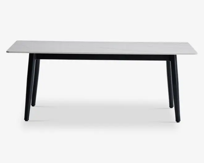 Rektangulært bord med en glat, hvid bordplade, der har et diskret marmorlignende mønster. Bordet har fire let skråtstillede, solide sorte ben, hvilket giver det et moderne og minimalistisk udtryk. Bordpladens kanter er lige og rene, og det samlede design er slankt og nutidigt.