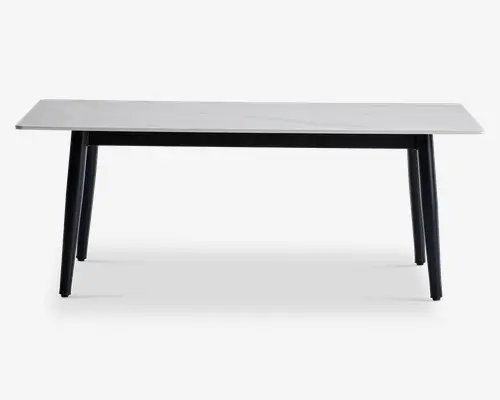 Rektangulært bord med en glat, hvid bordplade, der har et diskret marmorlignende mønster. Bordet har fire let skråtstillede, solide sorte ben, hvilket giver det et moderne og minimalistisk udtryk. Bordpladens kanter er lige og rene, og det samlede design er slankt og nutidigt.