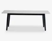 Rektangulært bord med en glat, hvid bordplade, der har et diskret marmorlignende mønster. Bordet har fire let skråtstillede, solide sorte ben, hvilket giver det et moderne og minimalistisk udtryk. Bordpladens kanter er lige og rene, og det samlede design er slankt og nutidigt.
