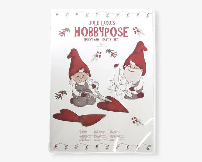 Emballagen har et festligt design med to tegneserie-nisser iført røde huer og grå tøj. Den ene nisse holder en saks og klipper et rødt hjerte ud, mens den anden samler en hvid papirstjerne. Baggrunden har små illustrationer af mistelten og danske flag, hvilket understreger juletemaet. Teksten på emballagen er på dansk og engelsk og angiver, at dette er et luksus jule-hobbykit. Udtrykket er legende og indbydende, velegnet til julehygge og kreative aktiviteter.