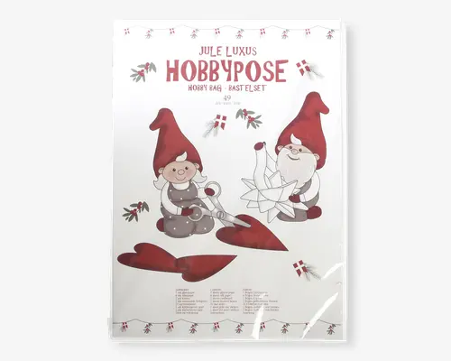Emballagen har et festligt design med to tegneserie-nisser iført røde huer og grå tøj. Den ene nisse holder en saks og klipper et rødt hjerte ud, mens den anden samler en hvid papirstjerne. Baggrunden har små illustrationer af mistelten og danske flag, hvilket understreger juletemaet. Teksten på emballagen er på dansk og engelsk og angiver, at dette er et luksus jule-hobbykit. Udtrykket er legende og indbydende, velegnet til julehygge og kreative aktiviteter.