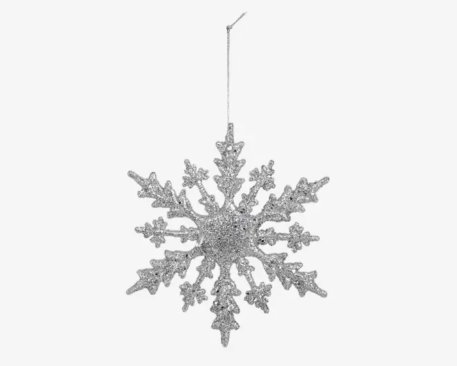 Et dekorativt ophængsornament formet som en snefnug, dækket af sølvglimmer for en glitrende effekt. Snefnugget har indviklede, symmetriske grene og en central kerne, med en tynd sølvsnor fastgjort øverst til nem ophængning. Overfladen er tekstureret og reflekterende, hvilket giver et festligt udseende.
