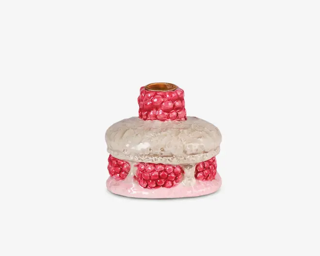 Lysestage i keramik med blank, tekstureret overflade. Hoveddelen er rund og offwhite med en let ujævn finish, dekoreret med hævede klynger af blanke lyserøde kugler, der er placeret i en ring omkring bunden og halsen. Den øverste åbning har en kant i metallisk guld, som giver et elegant og kontrastfuldt udtryk.
