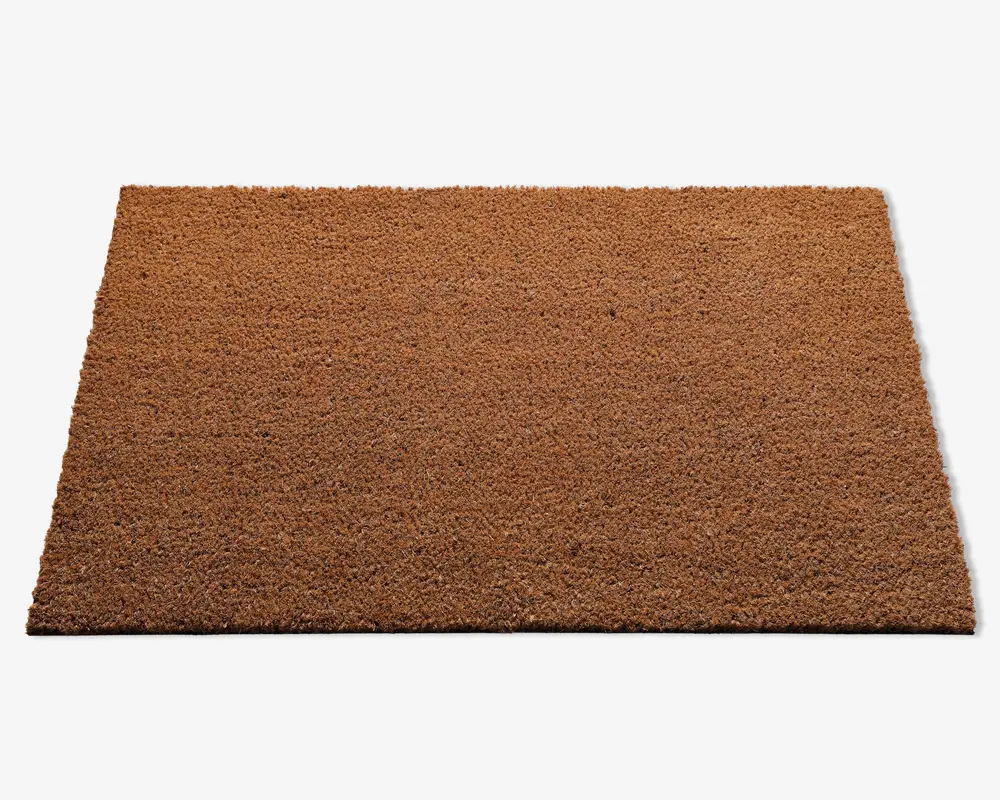 Rektangulær måtte med en grov, tekstureret overflade i en naturlig brun farve. Måtten ser ud til at være lavet af slidstærkt, fibret materiale, sandsynligvis kokos, og har rene, lige kanter. Den er ensfarvet uden mønstre eller design, velegnet til brug ved en indgang.