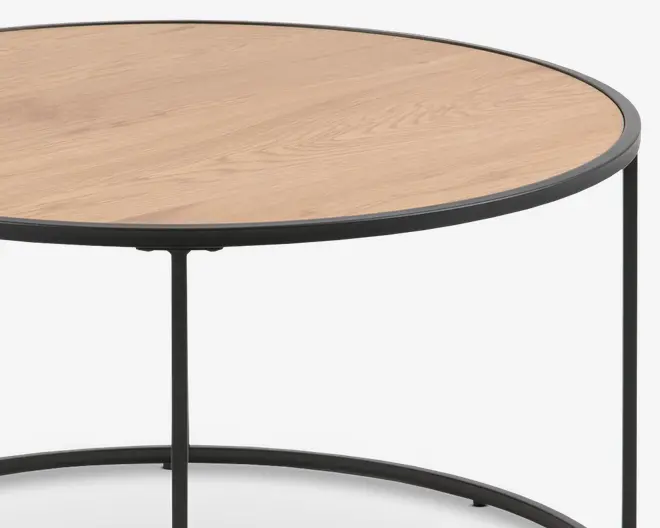 Rundt bord med en lys træbordplade og en tynd, sort metalramme. Bordpladen har en glat overflade, og benene er slanke og minimalistiske, forbundet af en cirkulær støtte nederst.
