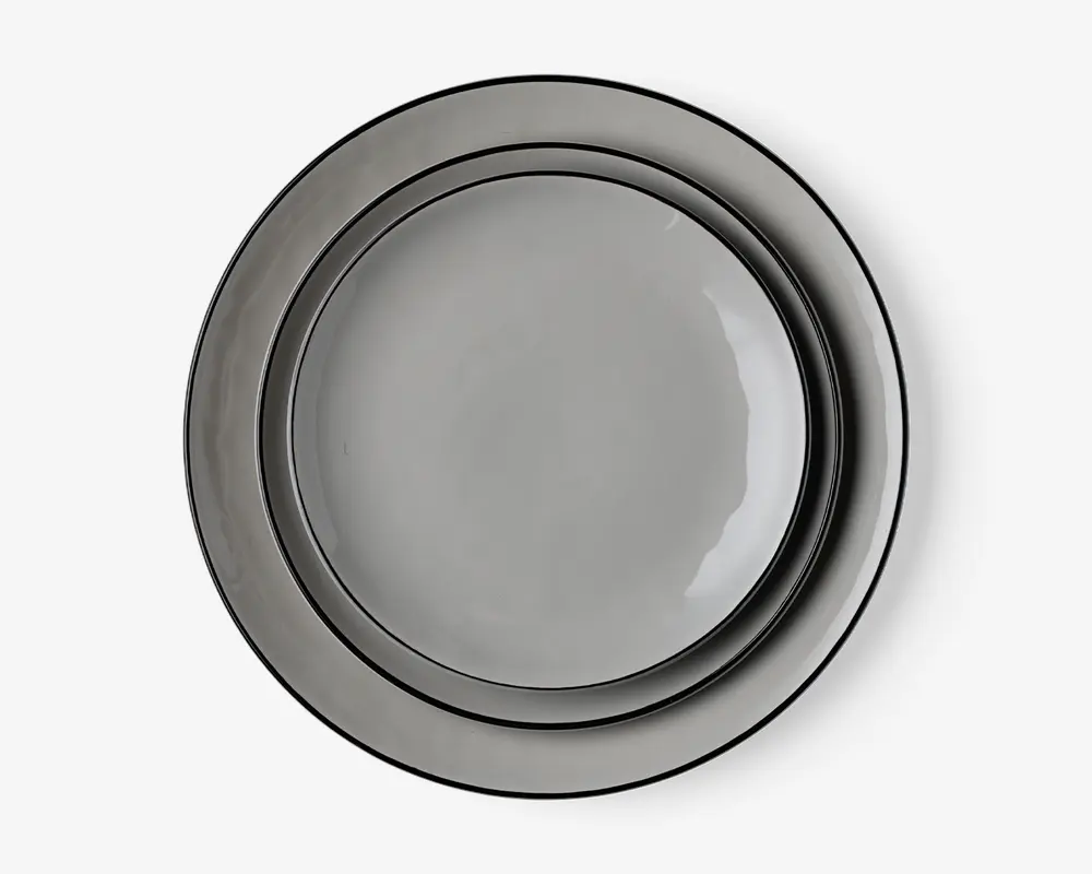 Sæt med tre runde tallerkener i forskellige størrelser, alle med en glat, blank grå overflade. Tallerkenerne har et minimalistisk design med let hævet kant og et diskret, moderne udtryk. Overfladerne er jævne og reflekterende, hvilket giver dem et stilrent udseende.