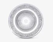 Rund tallerken med et indviklet, symmetrisk mønster. Midten har et strålende stjernemønster, omgivet af et bånd med geometriske motiver. Den brede kant er dekoreret med udsmykkede blomster- og rulleornamenter, hvilket giver tallerkenen et elegant og detaljeret udseende. Overfladen har en reflekterende, metallisk finish.