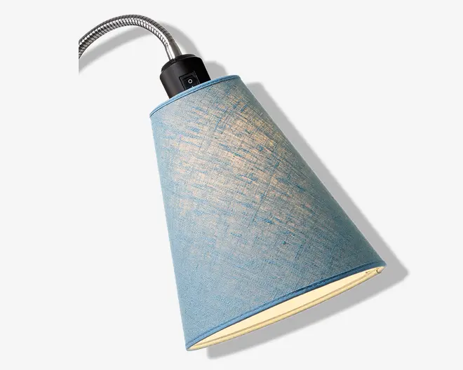 Denne lampe har en konisk lampeskærm beklædt med lyseblåt stof med en let tekstur og diskrete krydsskraveringer. Skærmen er monteret på en fleksibel, metal gooseneck-arm, som gør det muligt at justere lampens position. Lampen har en sort plastikfatning foroven med en synlig tænd/sluk-knap, hvilket gør den nem at betjene.