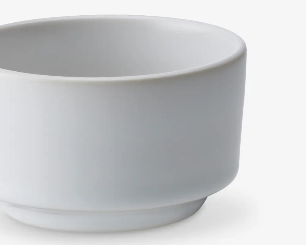 En lille, rund, hvid keramikskål med en glat, mat overflade. Skålen har lige sider og en let hævet bund, hvilket giver den et moderne og minimalistisk udtryk. Kanten er let buet, og designet er enkelt uden dekorationer.
