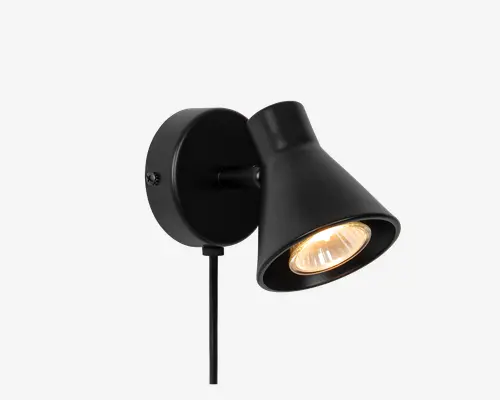 Væghængt lampe med mat sort finish og en konisk skærm, der leder lyset nedad. Lampen har en rund base og et justerbart hoved, så lyset kan rettes i forskellige retninger. Den synlige pære udsender et varmt skær, og der går en ledning ud fra bunden af basen til strømtilslutning.