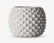 En rund, blank hvid keramisk beholder med en geometrisk, diamantmønstret tekstureret overflade. Ydersiden har hævede, pyramideformede former, der skaber en tredimensionel effekt. Toppen har en bred, glat åbning, og det samlede design er moderne og dekorativt.