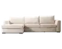 Moderne hjørnesofa med venstrevendt chaiselong, polstret i et lyst beige stof. Sofaen har tre store, bløde ryghynder og tre tykke sædehynder for ekstra komfort. Armlænene er brede og let afrundede, og designet er enkelt og minimalistisk, hvilket passer godt til moderne indretning.