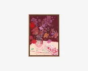 Et indrammet blomsterbillede med mørk burgunder baggrund, der viser løst malede rosa og røde blomster i en vase på et lyst bord, med en lille kop og en mønstret bog i forgrunden.