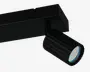 Justerbar cylindrisk spotlampe med mat sort finish og rillet overflade, der giver bedre greb og varmeafledning. Lygtehovedet har flere små LED-pærer arrangeret i en cirkel bag et klart dæksel, hvilket giver fokuseret og energieffektiv belysning. Lampen er monteret på en rektangulær skinne, hvilket muliggør fleksibel placering langs skinnesystemet.