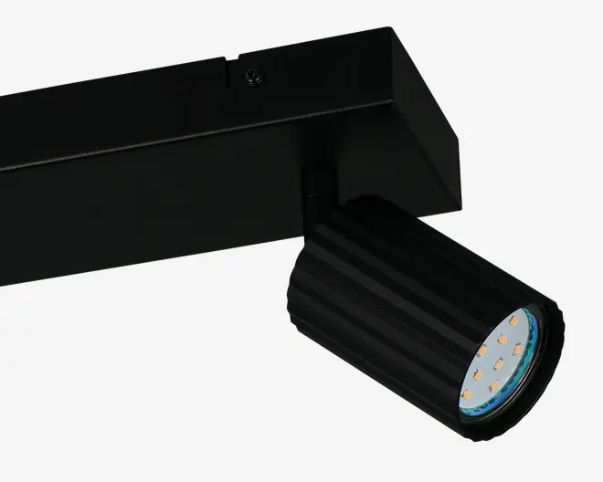 Justerbar cylindrisk spotlampe med mat sort finish og rillet overflade, der giver bedre greb og varmeafledning. Lygtehovedet har flere små LED-pærer arrangeret i en cirkel bag et klart dæksel, hvilket giver fokuseret og energieffektiv belysning. Lampen er monteret på en rektangulær skinne, hvilket muliggør fleksibel placering langs skinnesystemet.