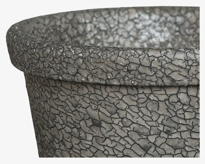 Nærbillede af en rund beholder med bred kant, der har en tekstureret overflade, som ligner revnet, forvitret sten. Farven er grå med mørke linjer, der fremhæver revnerne og giver et rustikt og gammelt udseende.