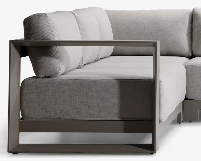Sektion af en moderne sofa med lysegrå, teksturerede stofhynder og en solid metalramme med mat finish. Armlænet og bunden er kantede og åbne, hvilket giver et minimalistisk og moderne udtryk. Sæde- og ryghynderne er tykke og bløde for ekstra komfort.