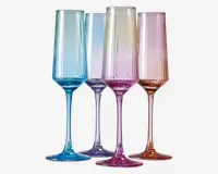 Sæt med fire høje, riflede glas med lodrette riller og en gradueret pastel farve. Hvert glas har sin egen nuance, herunder blå, lilla, pink og rav, hvor farven bliver mere intens mod bunden og stilken. Glassene har et moderne, elegant design med en slank stilk og en bred, stabil fod.