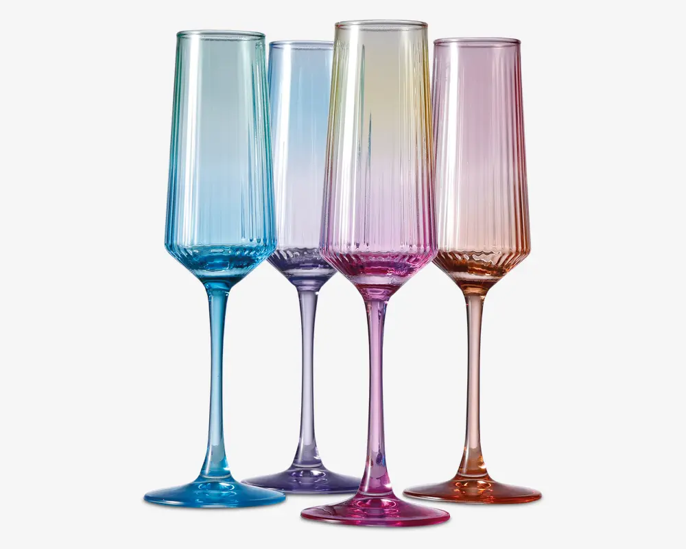 Sæt med fire høje, riflede glas med lodrette riller og en gradueret pastel farve. Hvert glas har sin egen nuance, herunder blå, lilla, pink og rav, hvor farven bliver mere intens mod bunden og stilken. Glassene har et moderne, elegant design med en slank stilk og en bred, stabil fod.