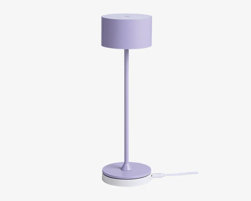 Høj, slank lampe med cylindrisk lampeskærm og fod, alt i en blød pastel-lilla farve. Lampen har et minimalistisk design med glatte overflader og rene linjer, velegnet til moderne indretning.