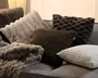 Assorterede pyntepuder med bløde, pelsagtige teksturer i creme, grå, mørkebrun, olivengrøn og hvid, arrangeret på en lysegrå sofa.