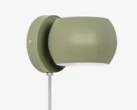 Væghængt lampe i mat olivengrøn med et afrundet, moderne design. Lampen har en glat, buet skærm, der leder lyset nedad, og en rund base med en synlig skrue til montering. En ledning går ud fra bunden af basen, hvilket indikerer, at lampen tilsluttes med stik i stedet for fast installation.