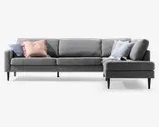 Grå L-formet hjørnesofa med chaiselong på højre side, lave ryghynder, slanke sorte ben og flere puder i pastelnuancer samt mønstret stof.