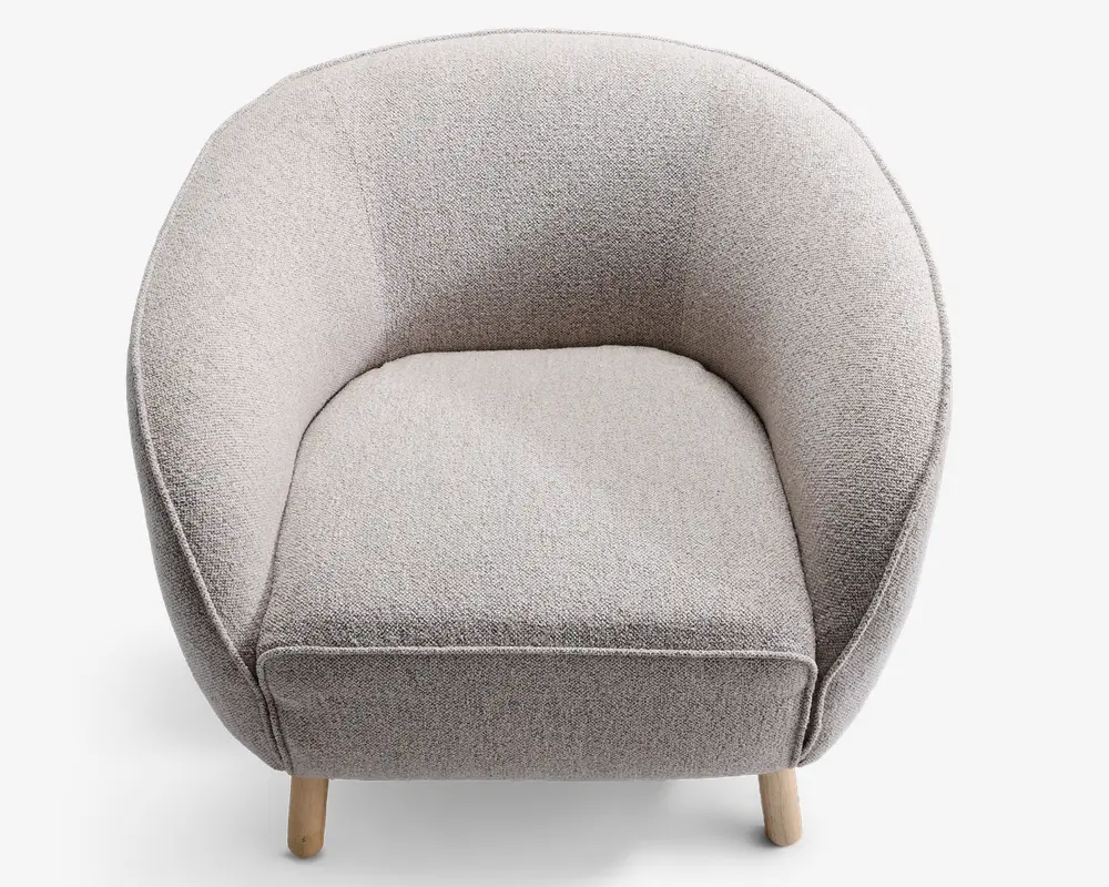 En moderne lænestol med rund ryg og sider, polstret med et lysegråt, tekstureret stof. Sædepuden er tyk og blød, hvilket giver god komfort. Stolen står på fire korte, lyse træben, hvilket giver et moderne og hyggeligt udtryk.