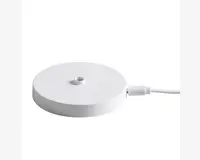 En rund, flad, hvid base med et lille centralt hul og en tilsluttet hvid strømkabel. Overfladen er glat og minimalistisk, og kablet er forbundet til siden af basen via et USB-stik.