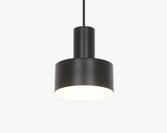 En moderne pendellampe med en mat sort cylindrisk metalskærm. Designet har en bredere nederste del og en smallere øverste del, hvilket giver en trinvist silhuet. Lampen hænger i en sort ledning, og undersiden er åben, så lyset skinner direkte nedad. Overfladen er glat, og stilen er minimalistisk, velegnet til moderne indretning.