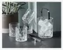 Sæt med fire klare, facetslebne glas med klassisk slibemønster, ledsaget af en matchende isspand fyldt med isterninger. Isspanden har et solidt metalhåndtag og leveres med en tang i metal. Glassene og spanden har en tung, elegant bund og en skinnende, tekstureret overflade, der reflekterer lyset.