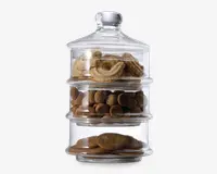 Klar, stabelbar glasbeholder med tre separate rum, hver fyldt med forskellige slags småkager. Øverste rum indeholder runde, snørklede smørsmåkager, midterste rum har små, runde chokoladekiks, og nederste rum har flade, ovale småkager. Beholderen har et tætsluttende låg med knop, som sikrer lufttæt opbevaring og holder indholdet frisk.