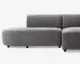 Moderne modulsofa med blødt, plysset gråt stofbetræk. Sofaen har en afrundet venstre armlæn og ryglæn, hvilket giver et glat og nutidigt udtryk. Sædehynderne er tykke og støttende, og sofaen står på korte, solide sorte ben. Designet er minimalistisk med rene linjer og uden synlige sømme eller udsmykninger.
