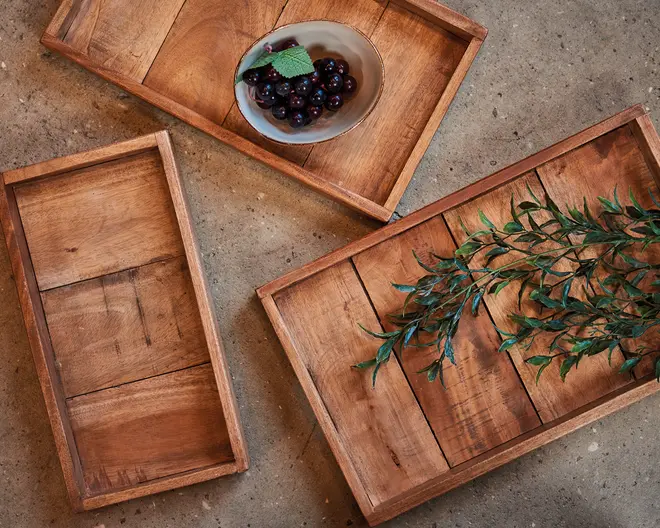 Sæt med tre rektangulære bakker i træ med forhøjede kanter, hver med synlig træstruktur og rustik finish. Bakkerne er vist i forskellige retninger, hvor den ene bakke har en lille skål med mørke bær og et mynteblad, og en anden bakke er pyntet med en grøn gren. Bakkerne har et solidt, håndlavet udseende med synlige samlinger i træet.