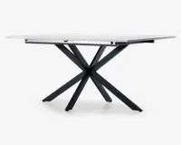 Rektangulært bord med en glat, hvid bordplade og en markant sort metalbase med fire skråtstillede ben, der krydser hinanden i midten og skaber et moderne, geometrisk udtryk. Bordet fremstår robust og har et stilrent design, der passer til forskellige indretninger.