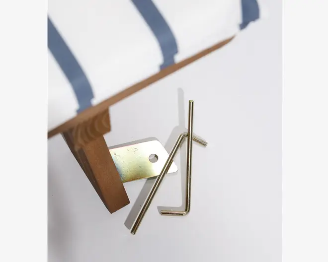 Nærbillede af et møbelben i træ, der er fastgjort med en metalbeslag, og to guldfarvede unbrakonøgler ligger ved siden af. Møblet har hvidt stof med blå striber. Billedet viser det medfølgende monteringsbeslag og værktøj til opsætning.