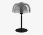 En moderne bordlampe med en rund, flad sort fod og en lige sort stang. Lampen har en kuppelformet, halvgennemsigtig skærm i røgfarvet glas, der dækker pæren og giver et stilrent og moderne udtryk. Designet er minimalistisk med rene linjer og en glat overflade.