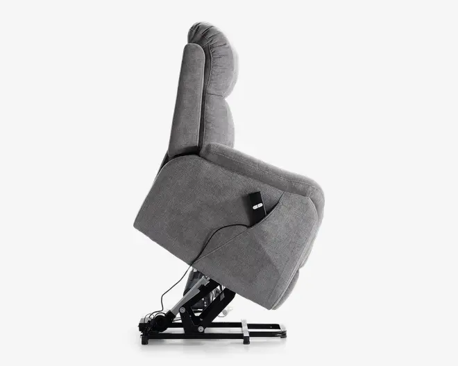 Sidevisning af en grå polstret reclinerstol i hævet position, hvor den metal løftemekanisme er synlig. Stolen har en polstret ryg, armlæn og sæde, med en fjernbetjening fastgjort på siden til nem justering. Stoffet ser blødt og tekstureret ud, hvilket giver komfort og støtte.