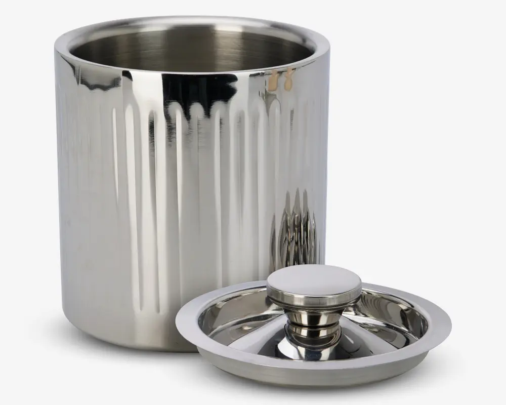En cylindrisk beholder i rustfrit stål med dobbeltvæg og blank, reflekterende overflade samt lodrette riller på ydersiden. Beholderen leveres med et matchende låg, der har et stort, rundt håndtag for nem afmontering. Indersiden er glat og sømløs, designet til at holde indholdet isoleret.