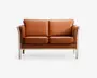 En moderne to-personers sofa, betrukket med glat, lysebrunt læder. Sofaen har bløde, aftagelige sæde- og ryghynder for ekstra komfort samt en solid, lystræsfyldt ramme med lige ben og let buede armlæn. Designet er minimalistisk og moderne, velegnet til forskellige stuer.