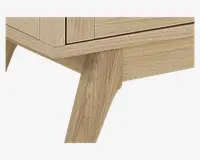 Nærbillede af et møbel med lys egetræsfinish og en glat, naturlig træstruktur. Billedet fremhæver et skråt, tilspidset ben og en enkel, moderne kant, hvilket indikerer en solid konstruktion og minimalistisk design.