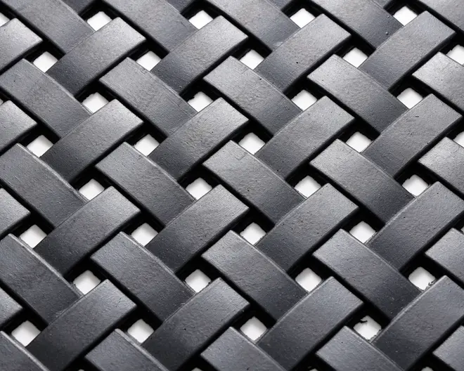 Nærbillede af et tæt vævet mønster lavet af flade, mat sorte strimler. Strimlerne er flettet sammen i et over-under kurveflet-design, hvilket skaber en tekstureret og holdbar overflade. Materialet virker robust, og vævningen er ensartet, hvilket giver både styrke og et moderne udtryk.