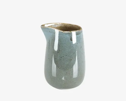 En lille keramikkande med rund krop og smal hældetud for nem udskænkning. Ydersiden har en blank, lyseblå glasur med små prikker, mens kanten og indersiden har en naturlig, uglaseret brun finish. Designet er minimalistisk og moderne, velegnet til servering af fløde, mælk eller saucer.